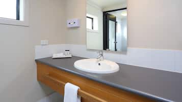 A bathroom with a white sink, a wooden vanity, a mirror, and a window.