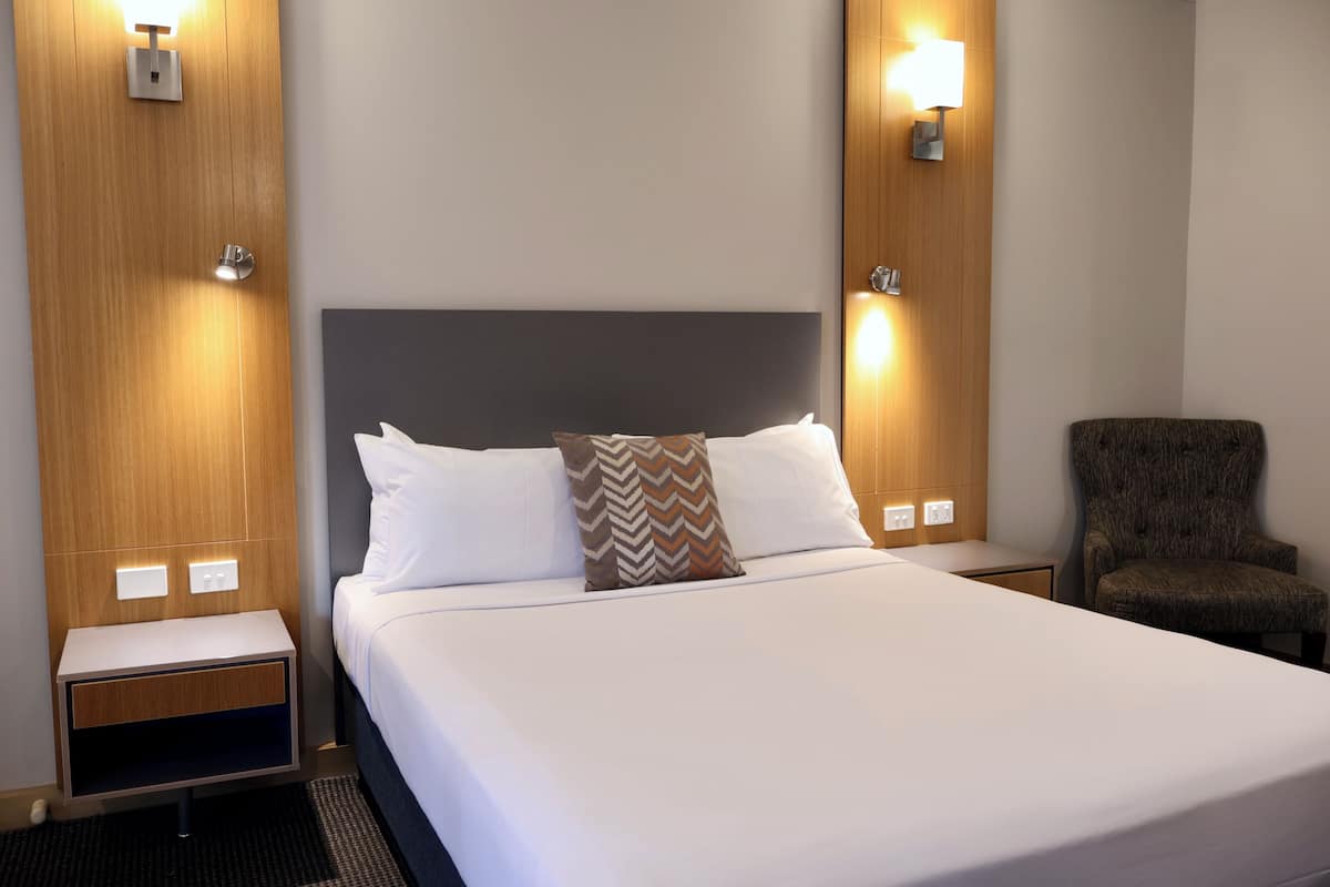 A hotel room with a bed, nightstands, a chair, and wall-mounted lights.