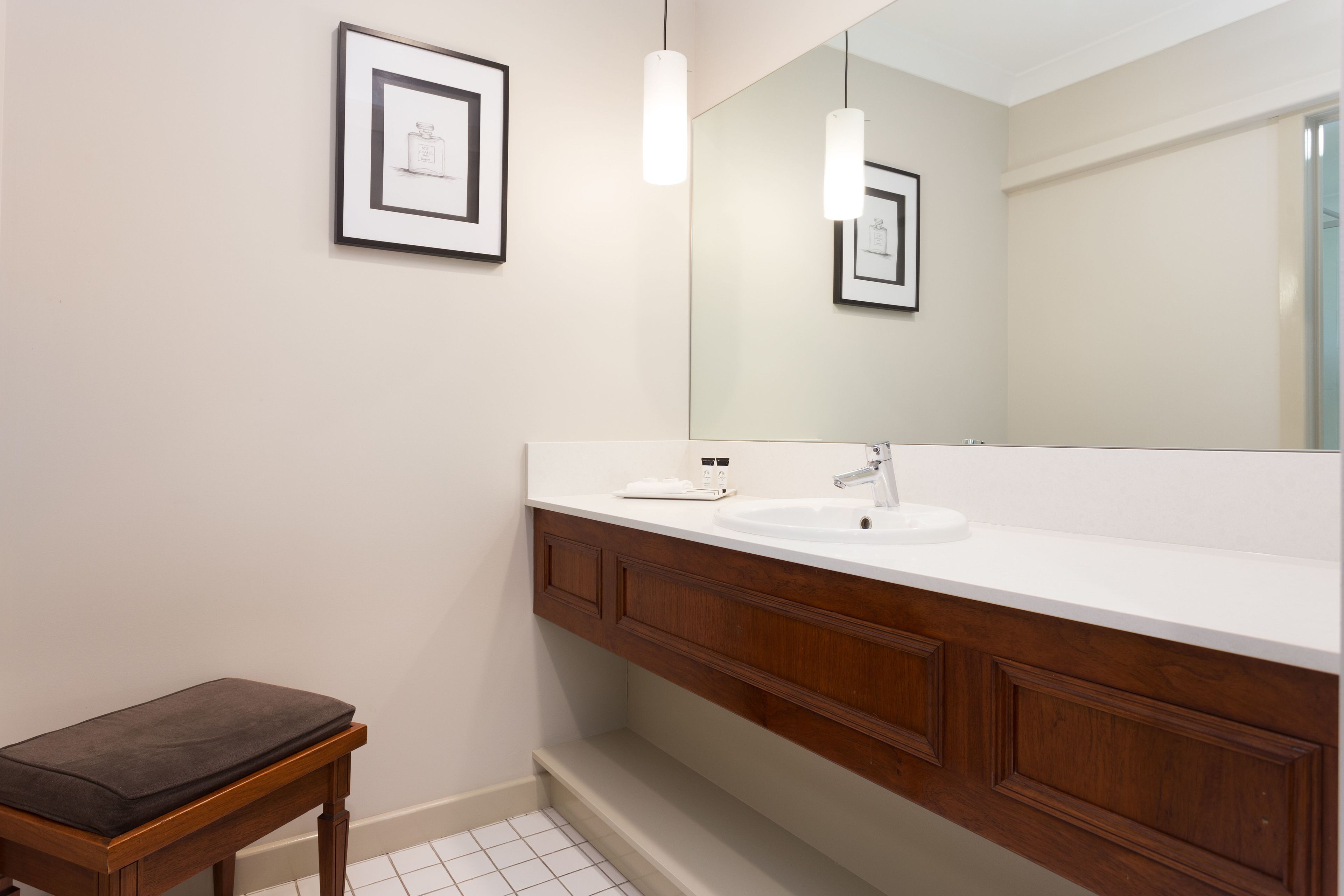 Une salle de bain moderne avec un grand miroir, un lavabo blanc, un meuble-lavabo en bois et un banc.