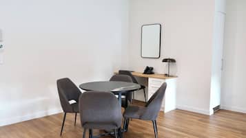 A modern room with a round table, four grey chairs, a desk with a computer, and a wall-mounted mirror.