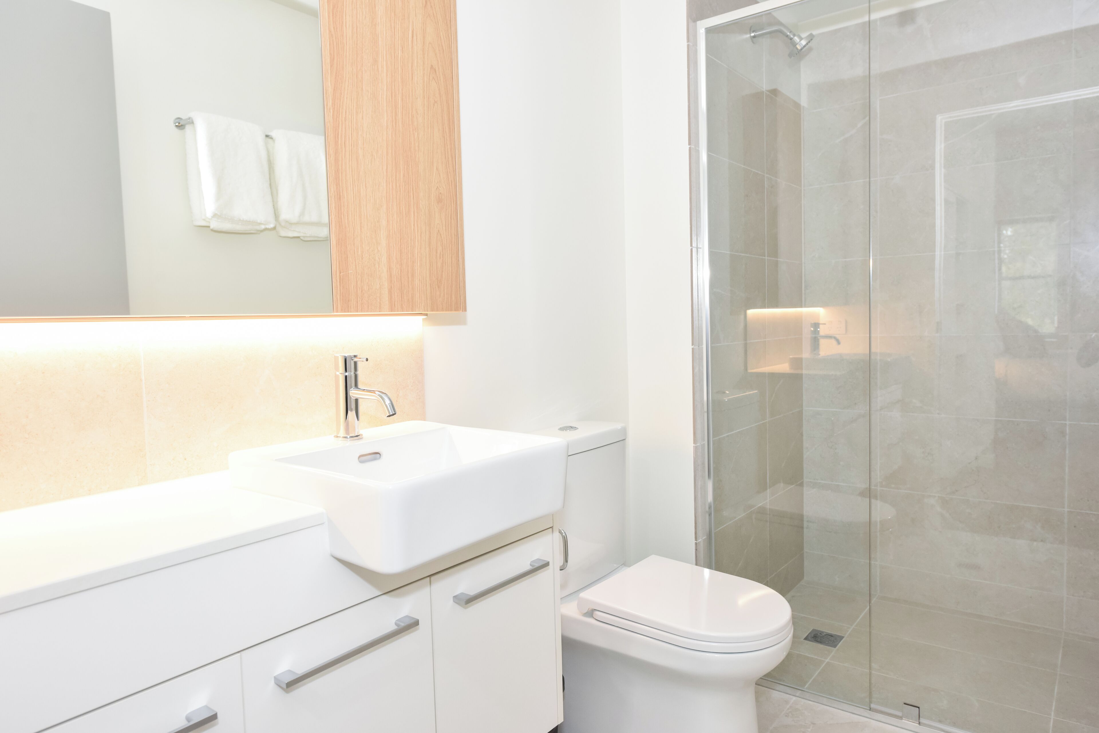 Un baño moderno con lavamanos, inodoro y cabina de ducha con mampara de vidrio.