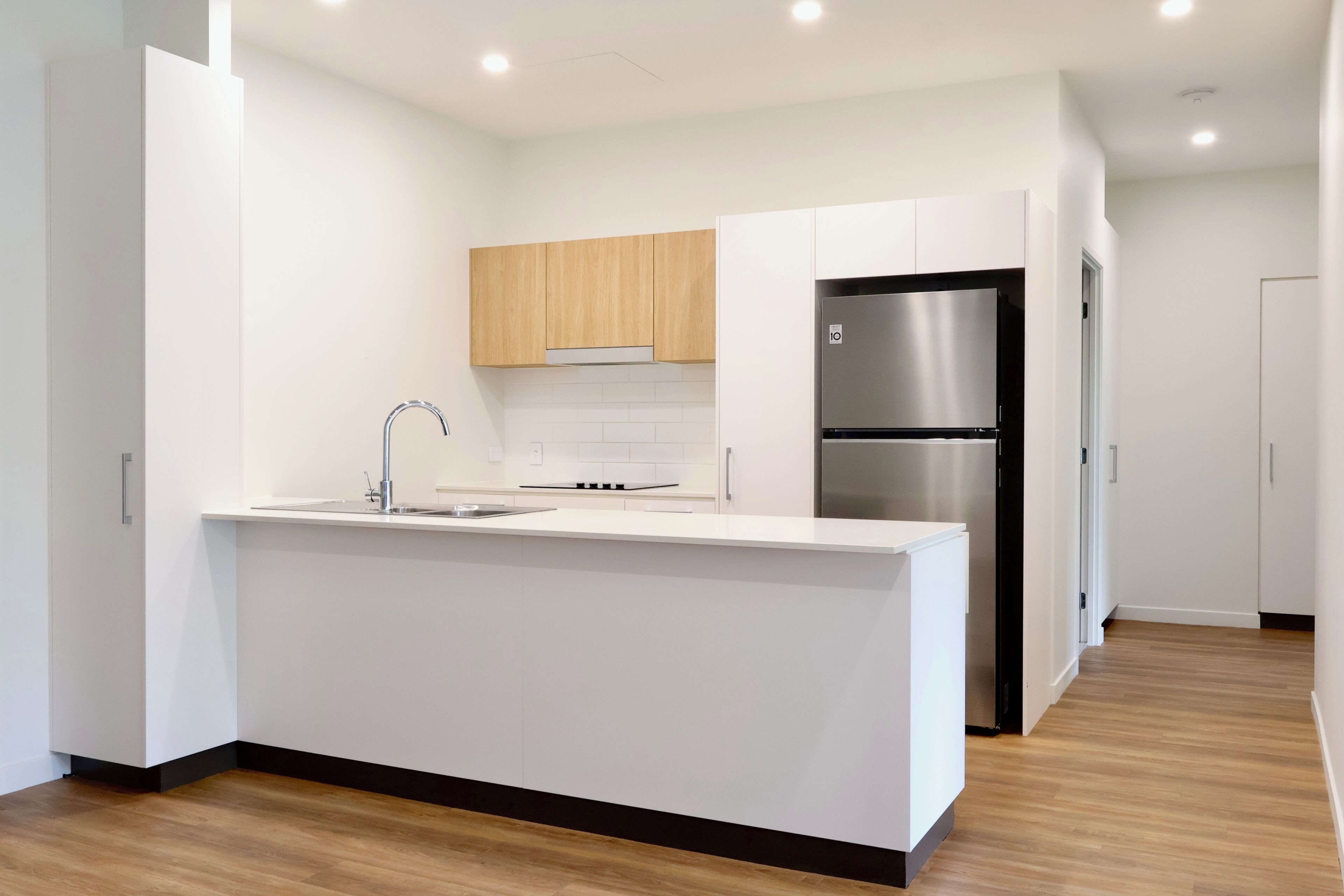 Cocina moderna con armarios blancos, refrigerador de acero inoxidable y encimera de madera.