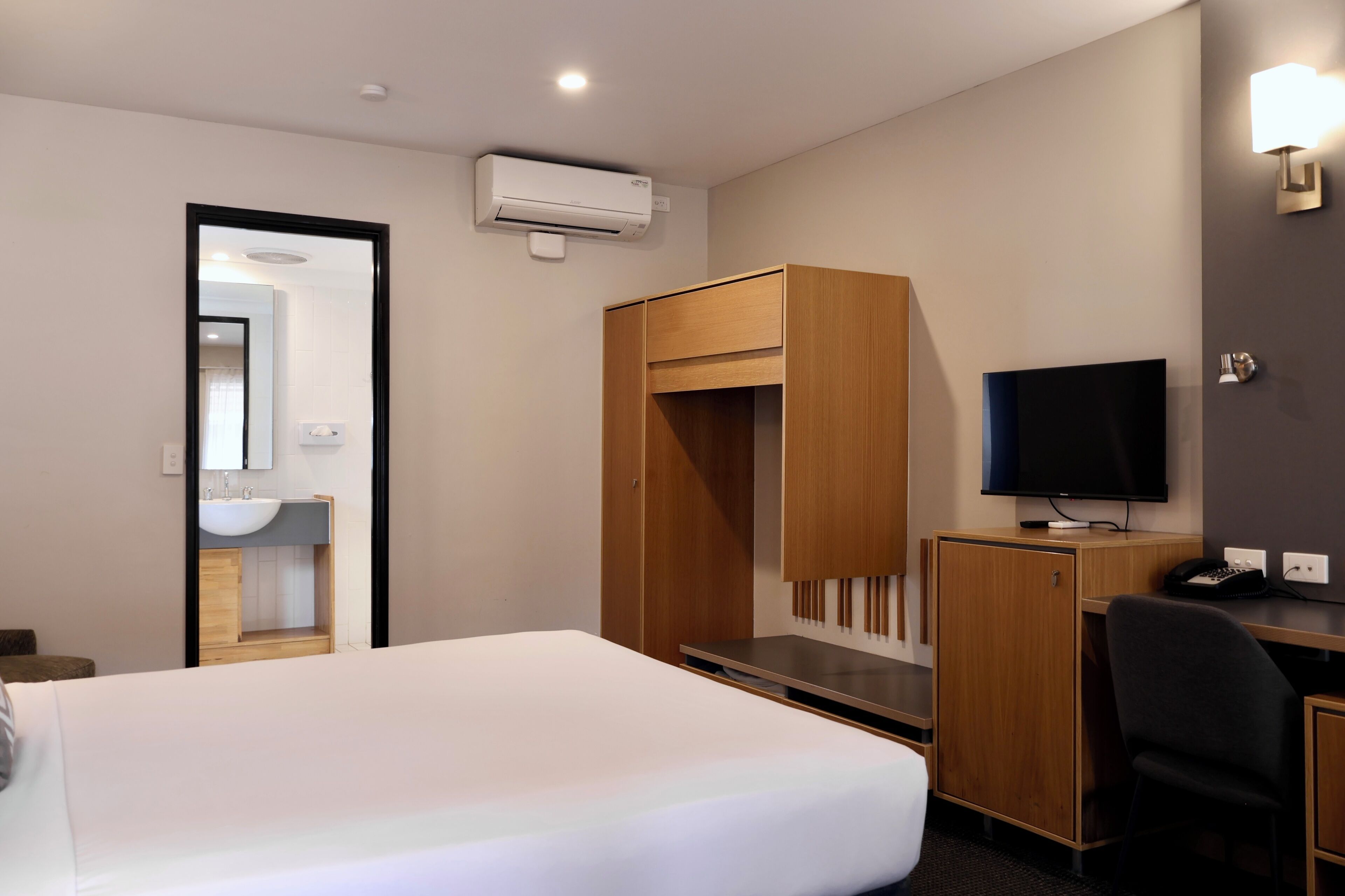 A hotel room with a bed, a desk, a television, a wardrobe, and a mirror.