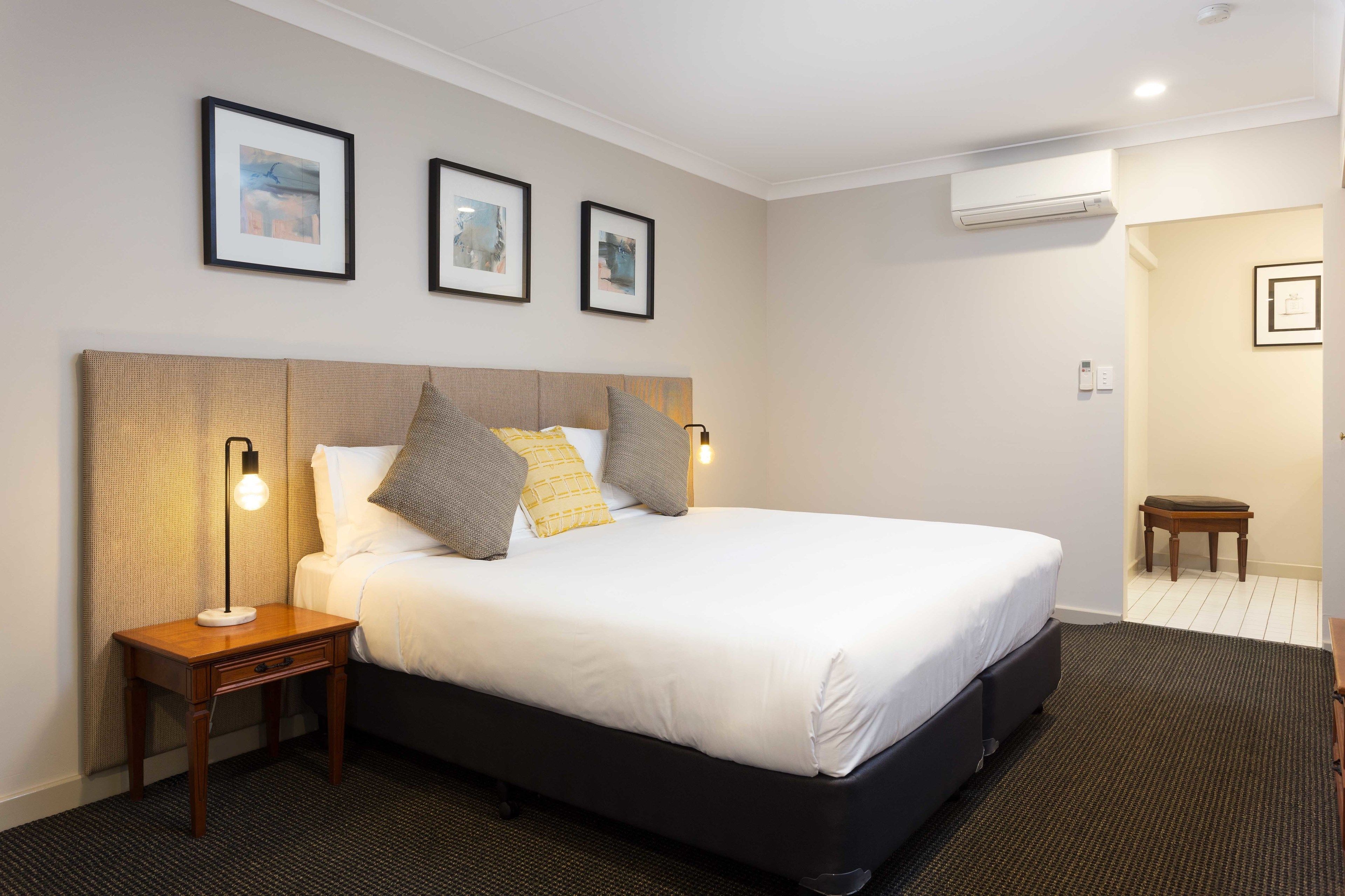 A neatly arranged hotel room with a large bed, bedside lamps, and framed pictures on the wall.