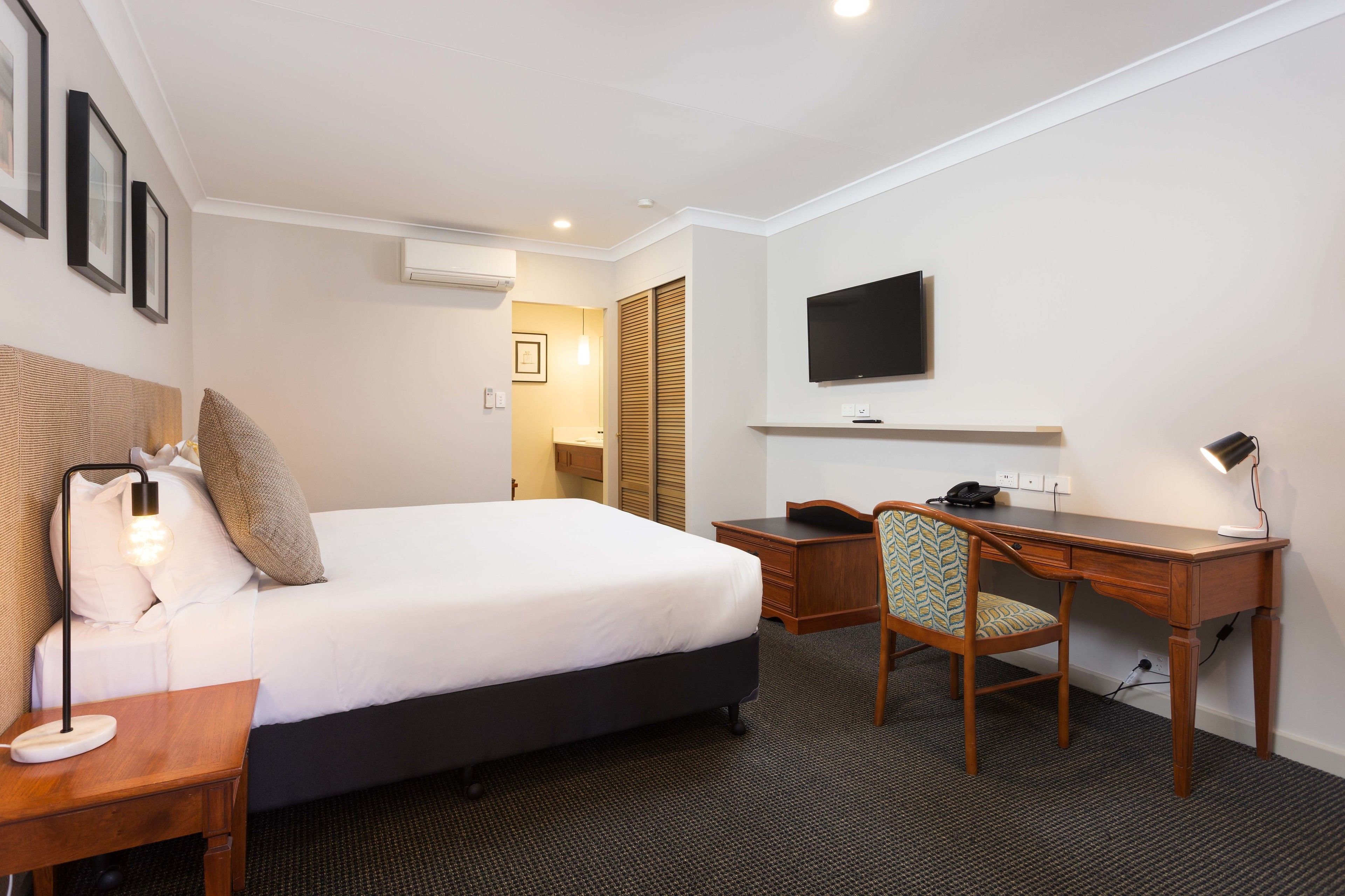A hotel room with a bed, desk, chair, and TV.