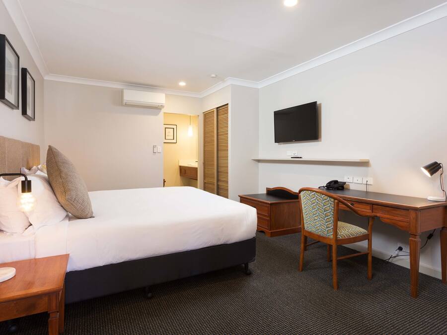 A hotel room with a bed, desk, chair, and TV.