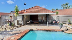A backyard with a swimming pool, patio furniture, and a covered seating area. - Brisbane International - Virginia (Boondall)