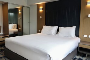 A modern hotel room with a large bed, a bedside table, a nightstand, a mirror, and a wall-mounted light fixture. - Brisbane International - Virginia (Boondall)