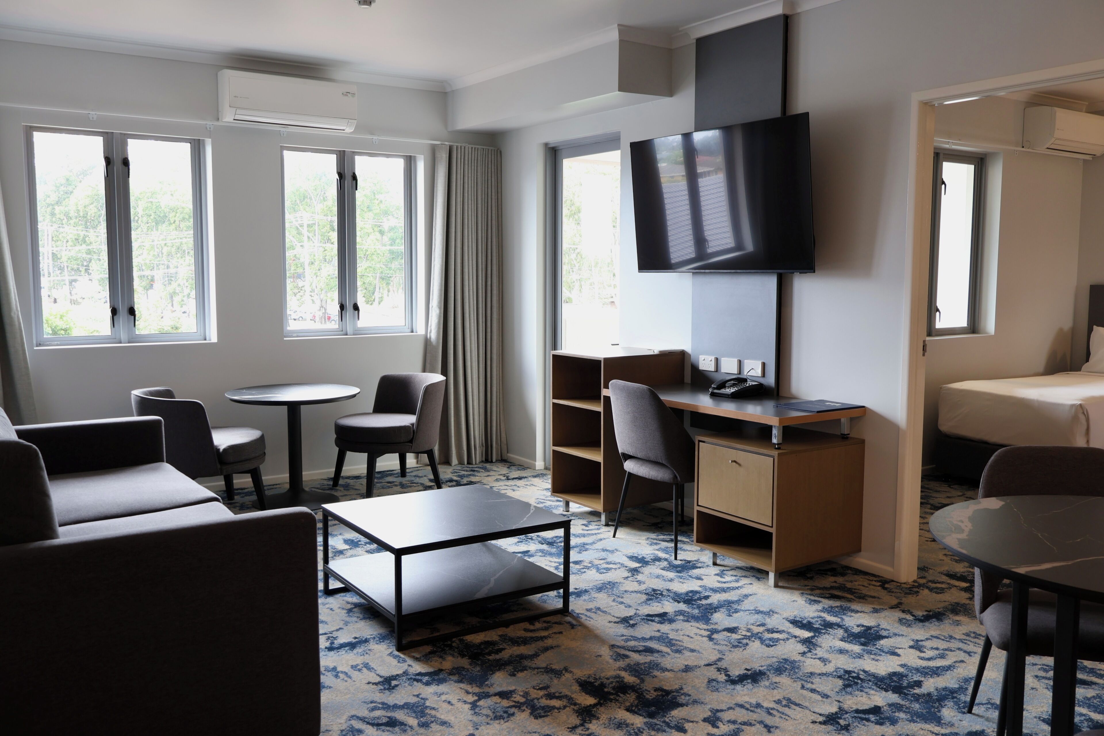 Quarto de hotel com cama, escrivaninha, televisão, sofá e duas cadeiras.