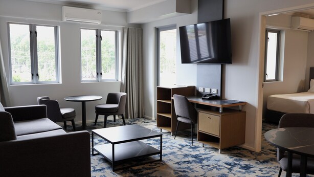 A hotel room with a bed, a desk, a TV, a sofa, and two chairs. - Brisbane International - Virginia (Boondall)