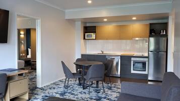 A compact living space with a kitchenette, a dining area with chairs, a sofa, and a flat-screen TV mounted on the wall.