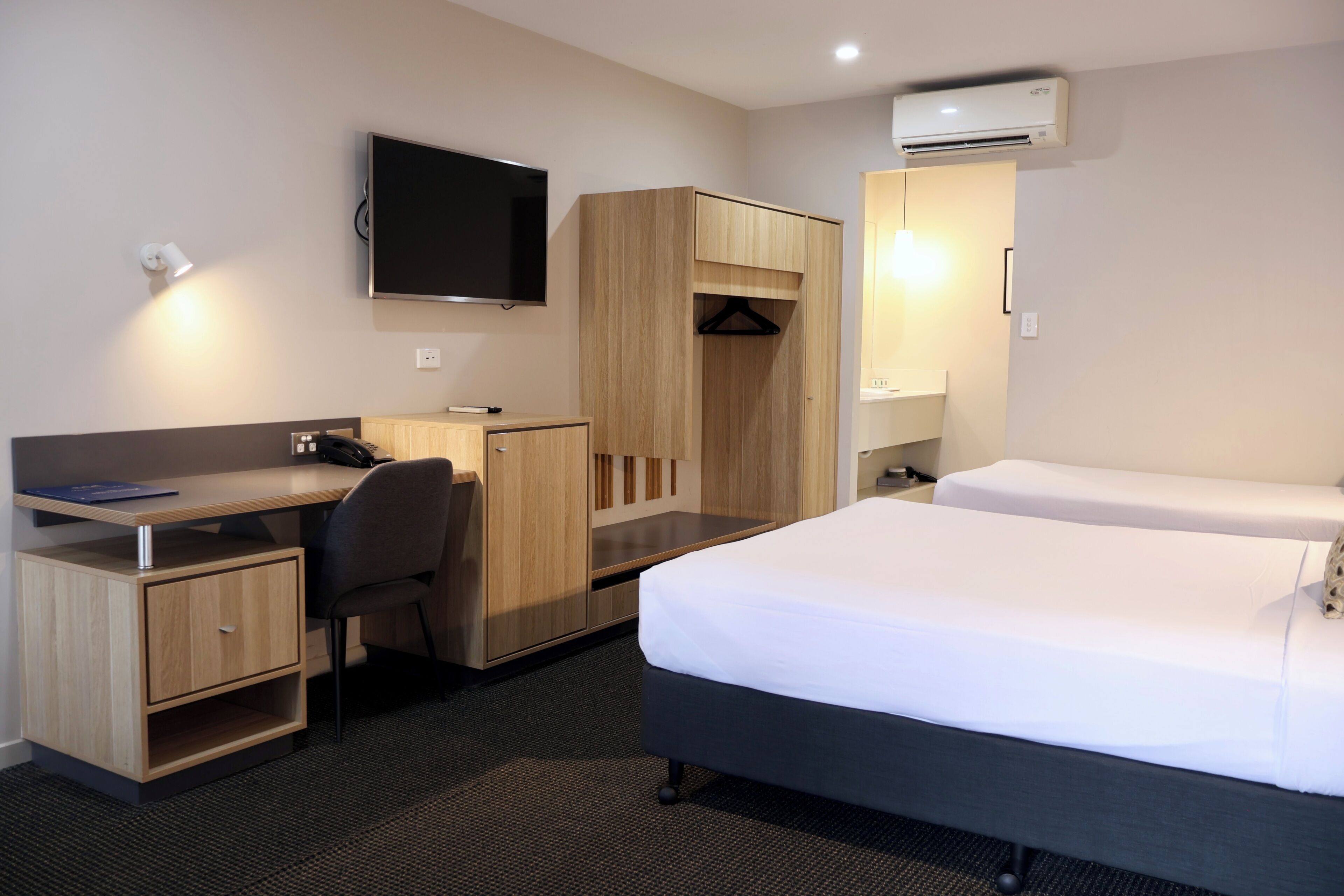 Une chambre d’hôtel équipée d’un lit, d’un bureau, d’une chaise, d’une armoire, d’un téléviseur et d’un appareil de climatisation.
