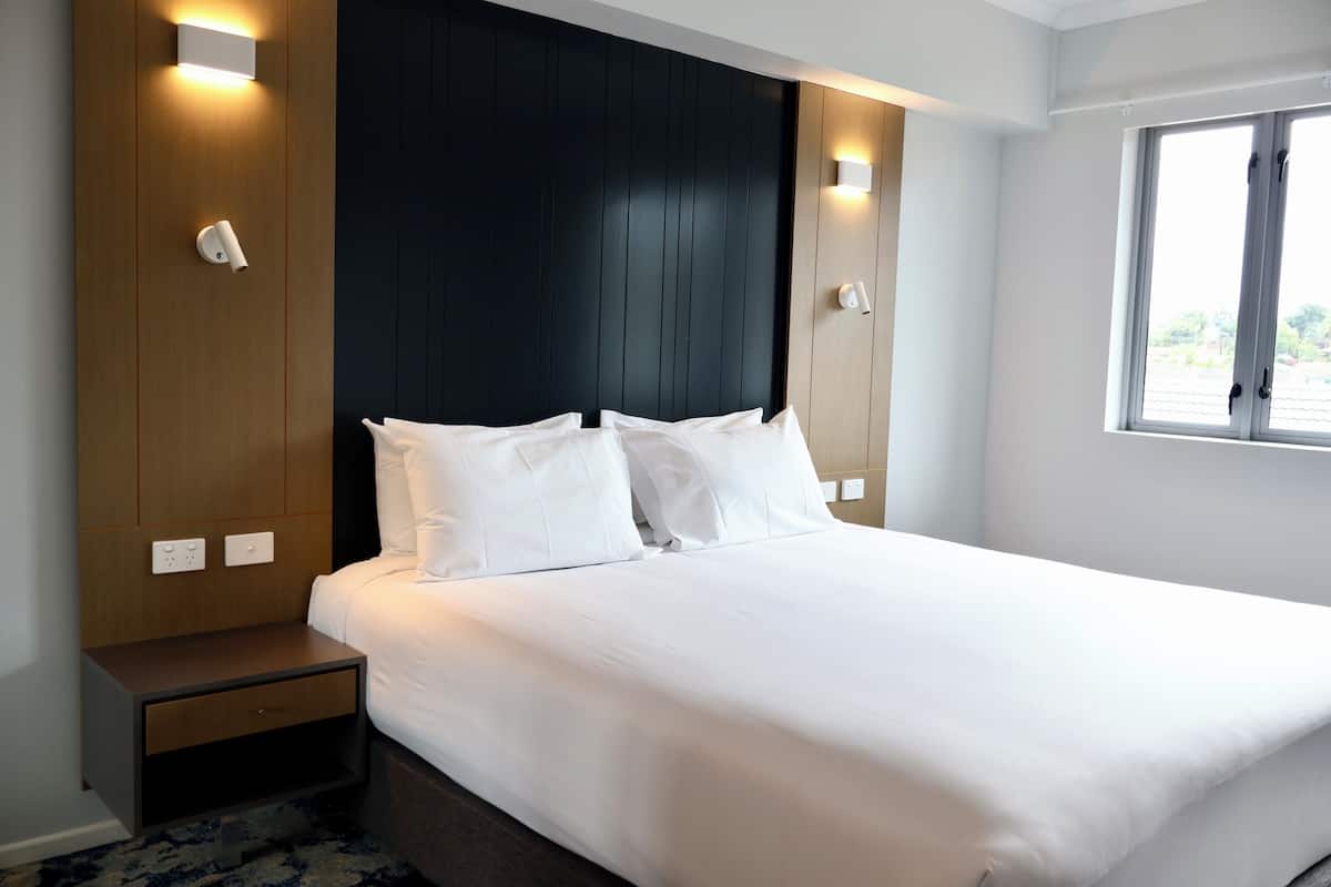 A hotel room with a large bed, a nightstand, a wooden panel wall, and a window.