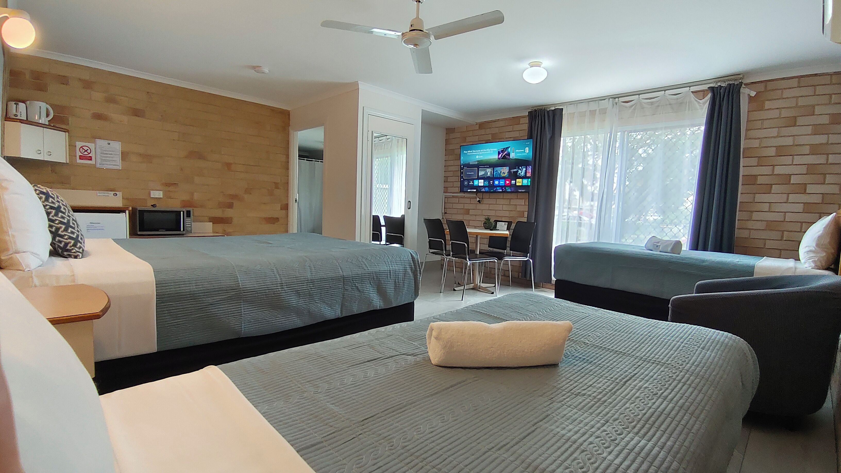 A hotel room with two beds, a desk, a television, and a ceiling fan.
