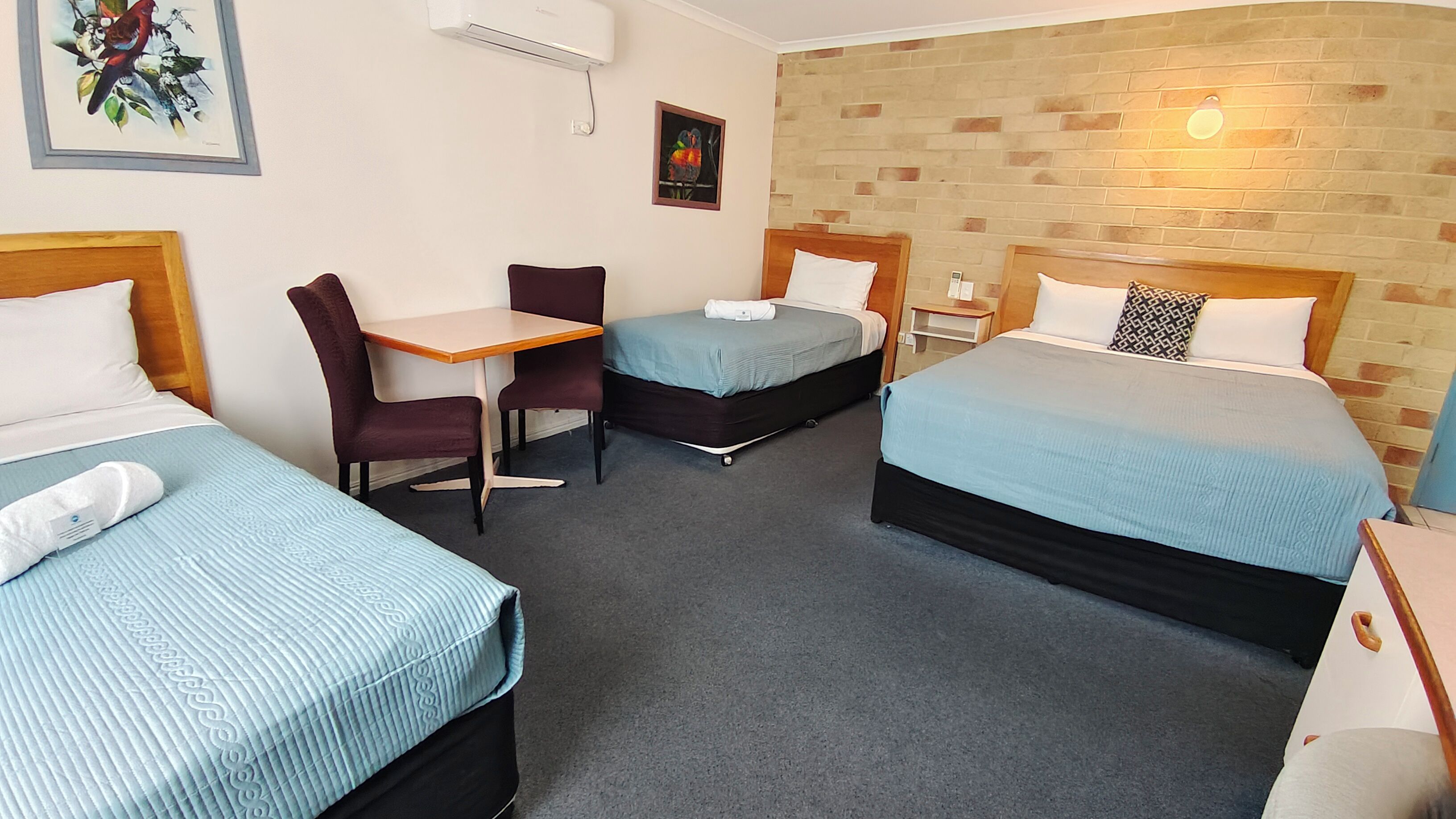 A hotel room with two single beds, a small table, two chairs, a desk, and a brick accent wall.