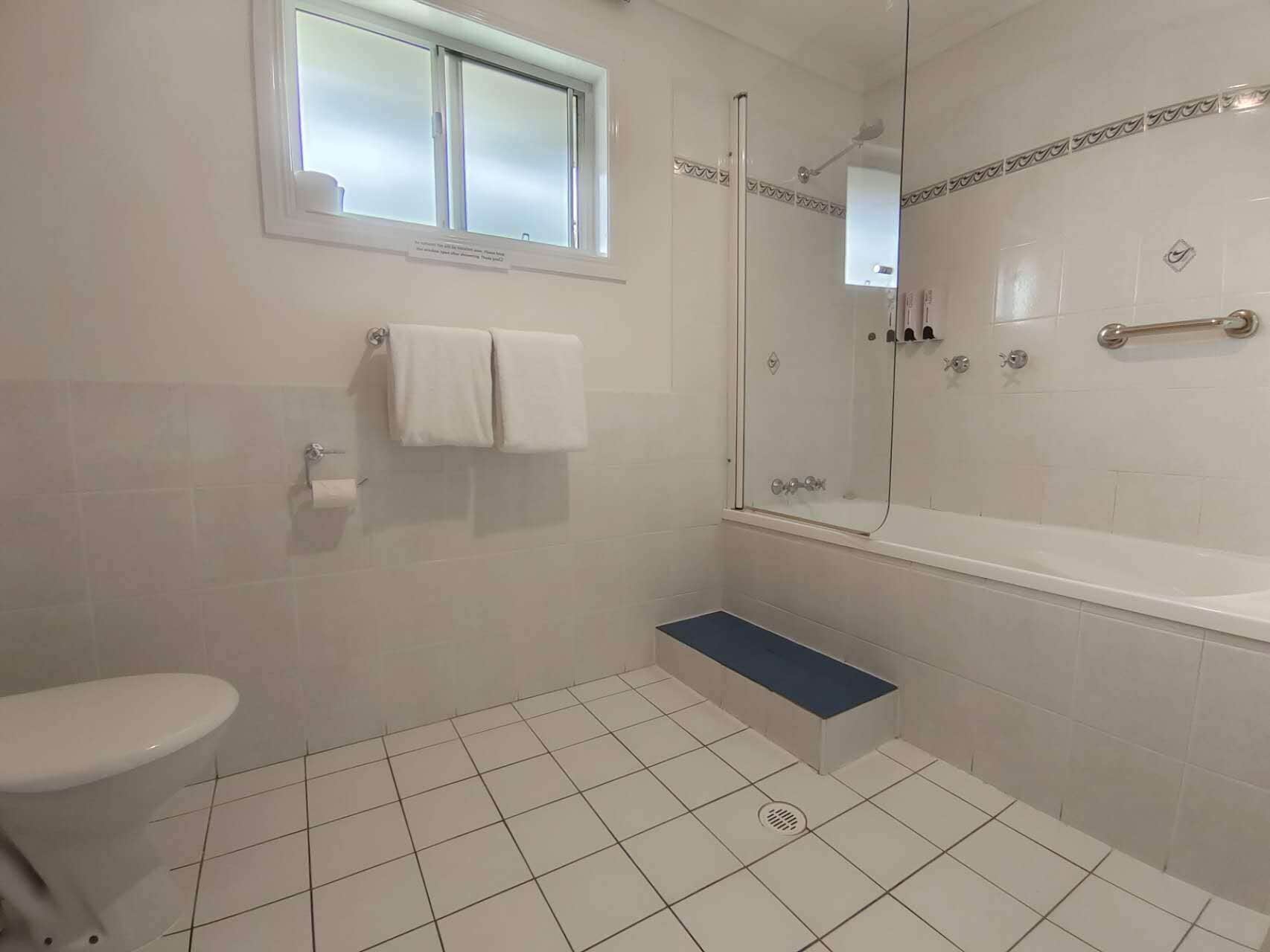 A bathroom with a toilet, a shower with a glass door, a bathtub, and a window.