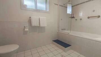 A bathroom with a toilet, a shower with a glass door, a bathtub, and a window.