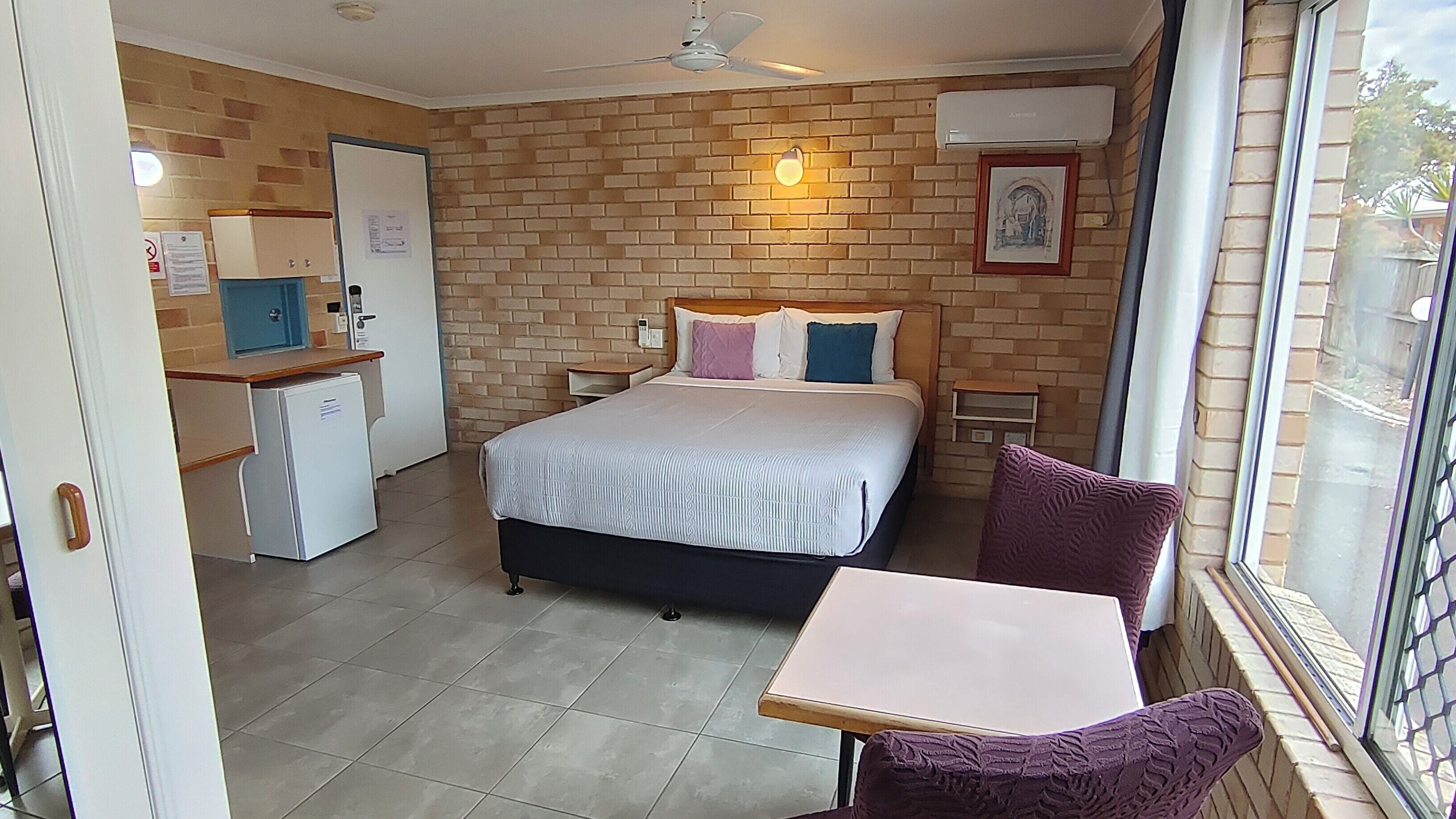 A bedroom with a bed, a desk, a chair, a window, and a door.
