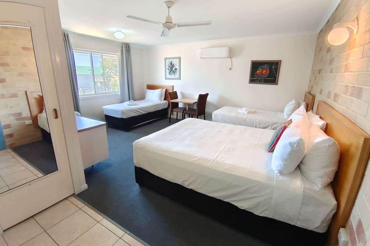 A hotel room with two single beds, a desk, a chair, a ceiling fan, and a window with curtains.