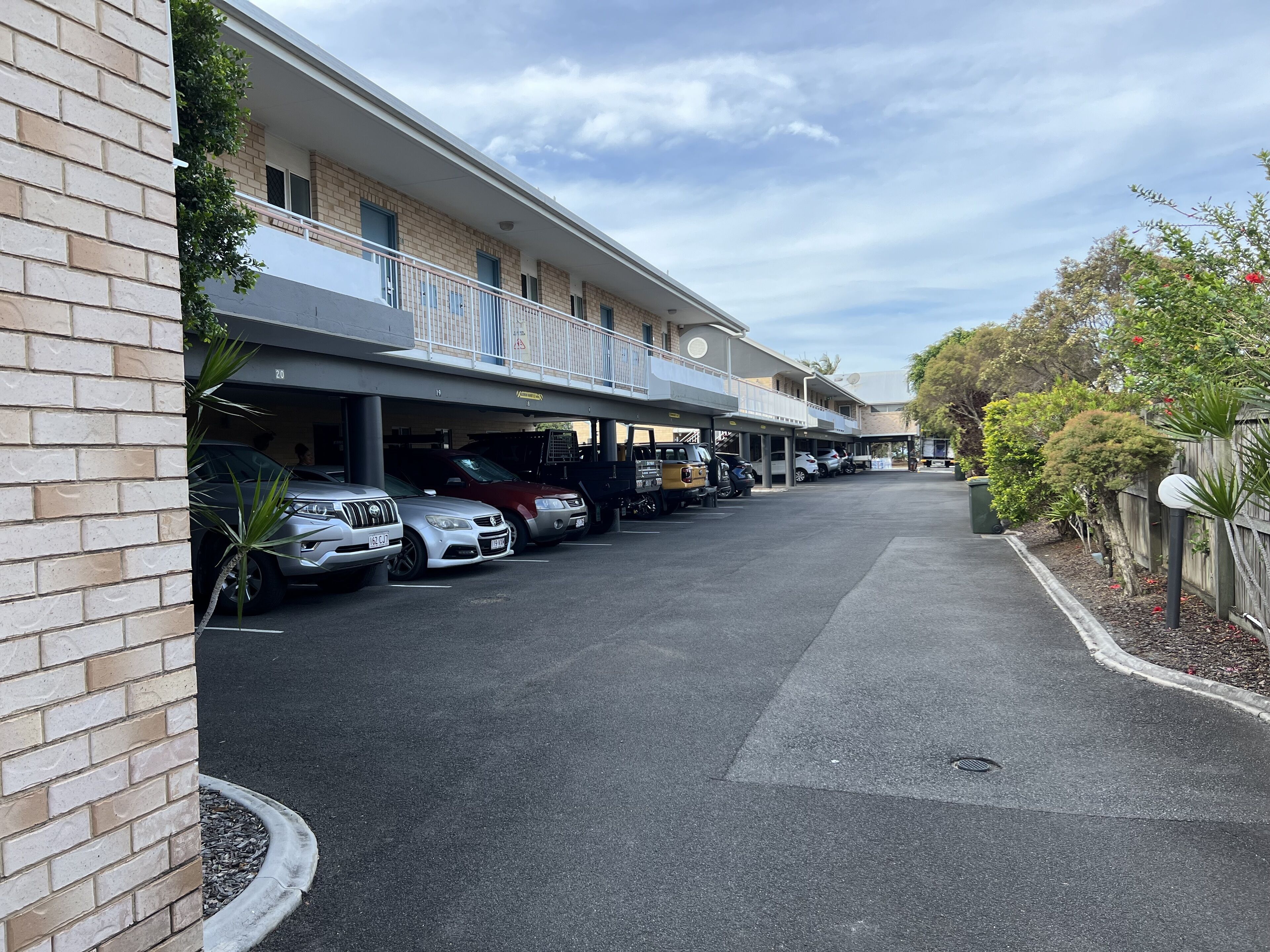 A parking area with multiple cars, a building with a balcony, and a clear sky.