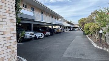A parking area with multiple cars, a building with a balcony, and a clear sky.