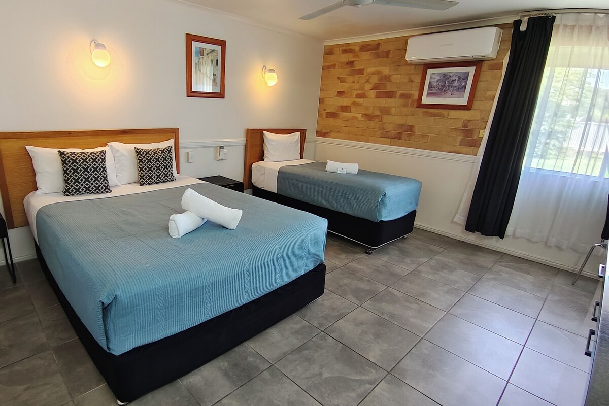 A hotel room with two beds, a small table, and a ceiling fan.