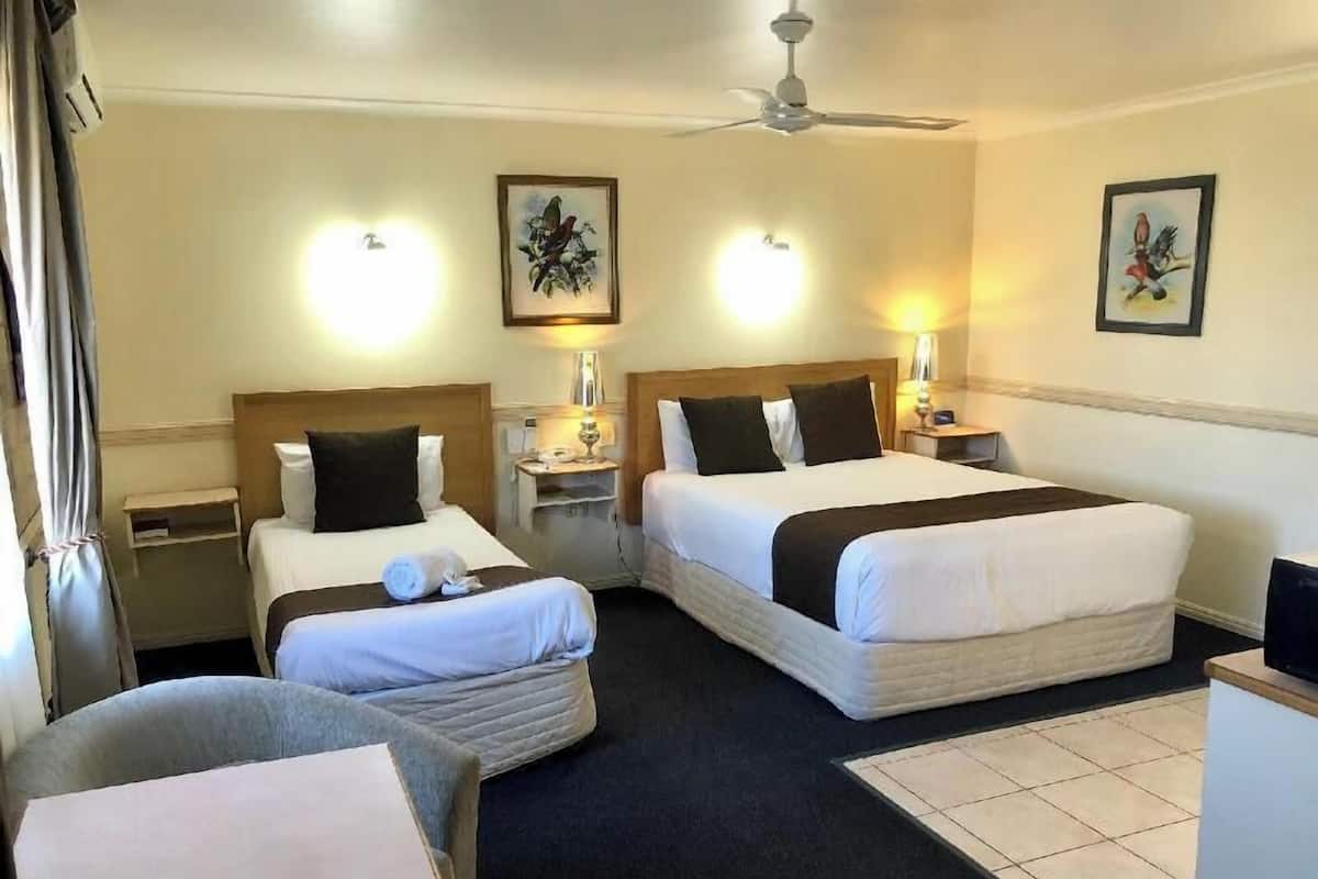A hotel room with two beds, a ceiling fan, bedside lamps, a small table, a chair, and artwork on the walls.