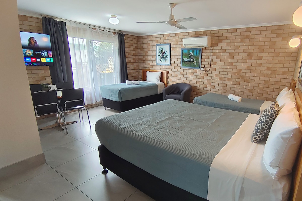 Habitación de hotel con dos camas, un escritorio, una silla, un televisor y obras de arte en la pared.