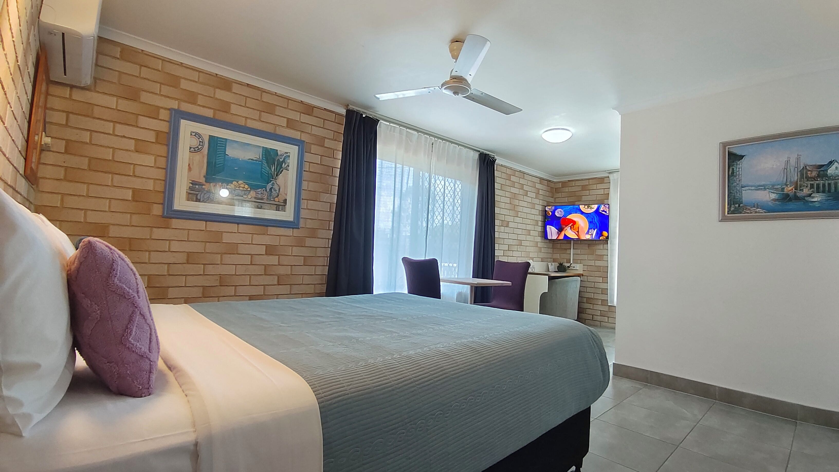 A hotel room with a bed, a desk with a chair, a television, and a ceiling fan.
