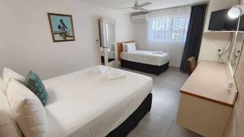 A hotel room with two beds, a desk, a ceiling fan, a TV, and a window with curtains.
