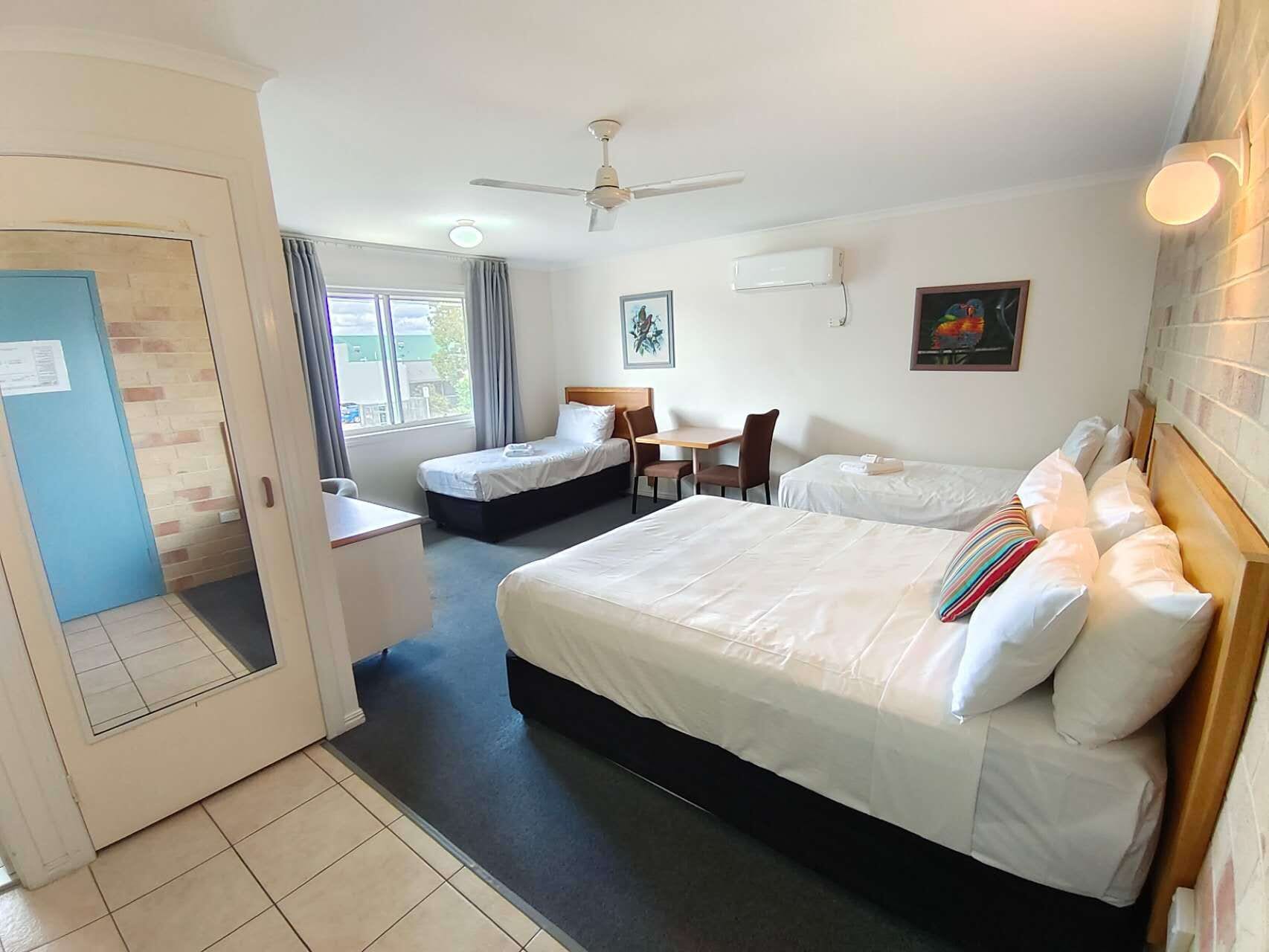 Een hotelkamer met twee bedden, een bureau, een stoel, een plafondventilator en een raam met gordijnen.