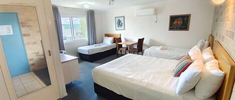 Habitación de hotel con dos camas, un escritorio, una silla, un ventilador de techo y una ventana con cortinas.