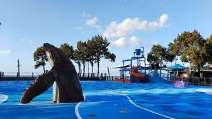 A swimming pool with a large sculpture, a lifeguard stand, and a blue deck area. - Ambassador Motor Lodge (Hervey Bay)