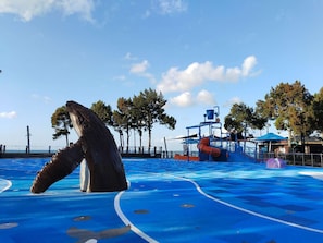 A swimming pool with a large sculpture, a lifeguard stand, and a blue deck area. - Ambassador Motor Lodge (Hervey Bay)