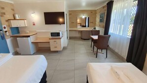 A hotel room with two beds, a desk, a microwave, a small refrigerator, a TV, and a dining area with chairs. - Ambassador Motor Lodge (Hervey Bay)
