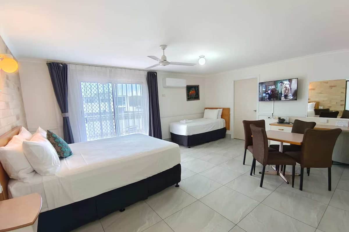 A hotel room with a large bed, a smaller bed, a dining area with chairs, a TV, and a ceiling fan.