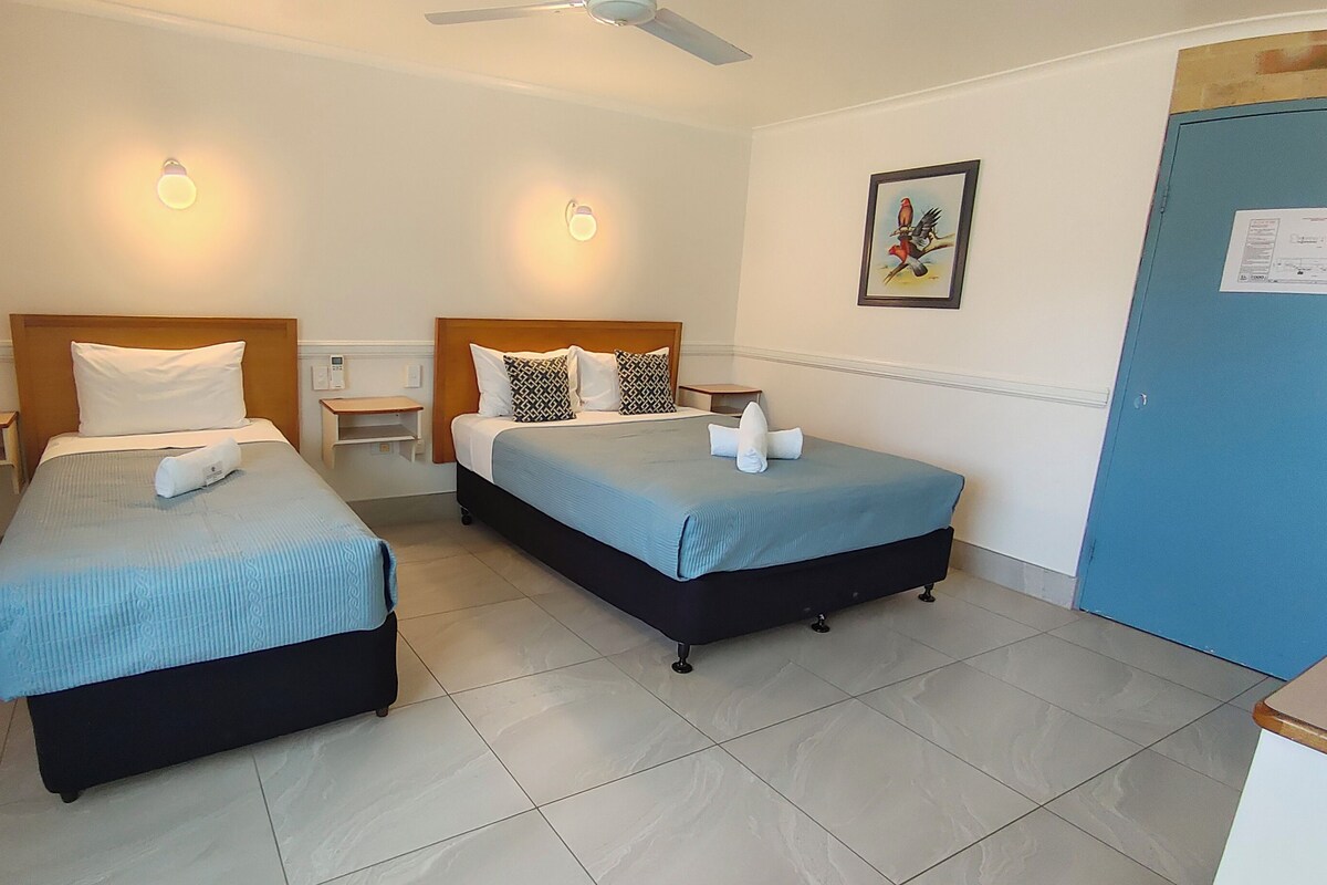 A hotel room with two beds, a ceiling fan, a nightstand, a wall-mounted light, and a door.