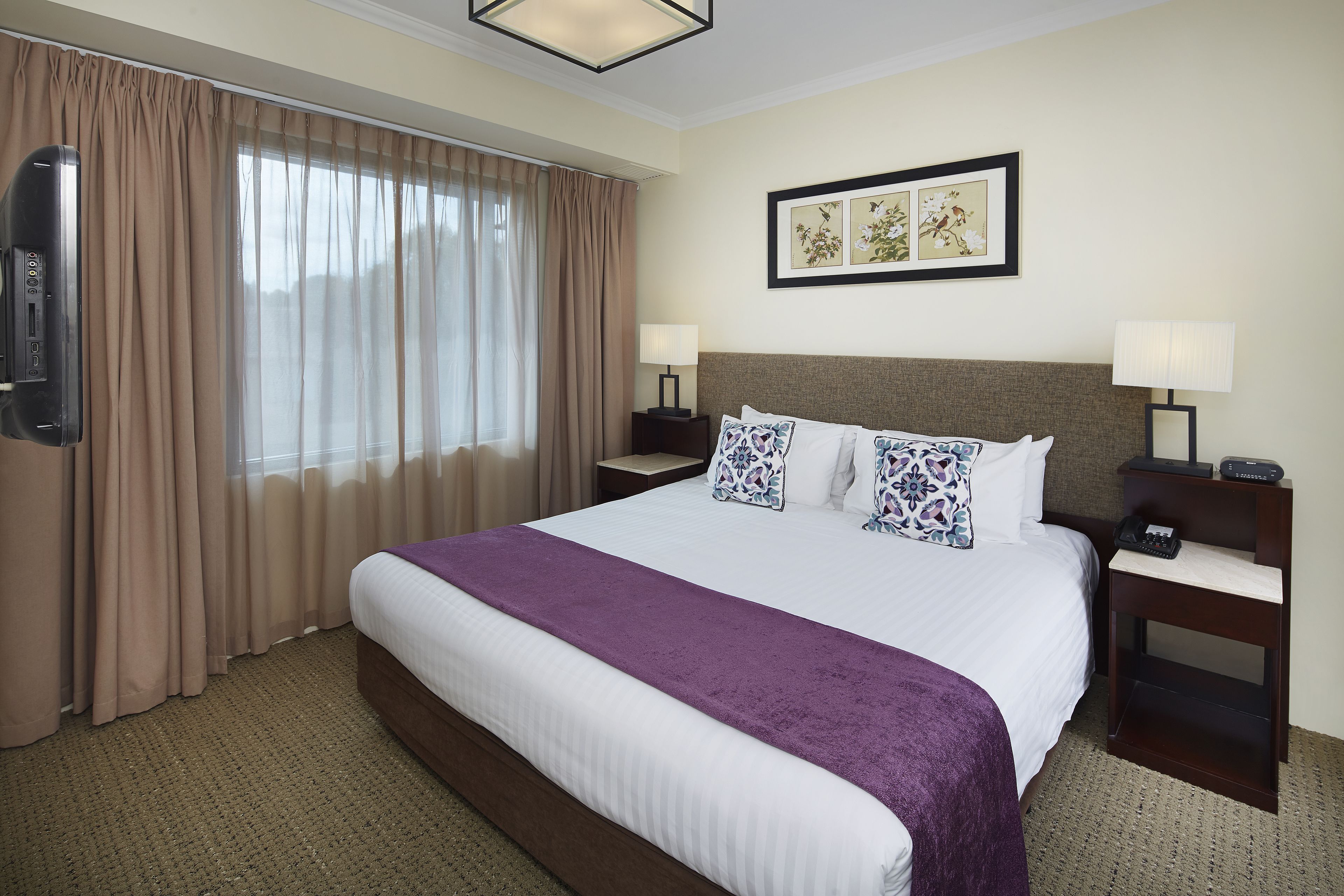 Quarto de hotel com uma cama grande, duas mesas de cabeceira com luminárias, uma televisão de tela plana e uma janela com cortinas.