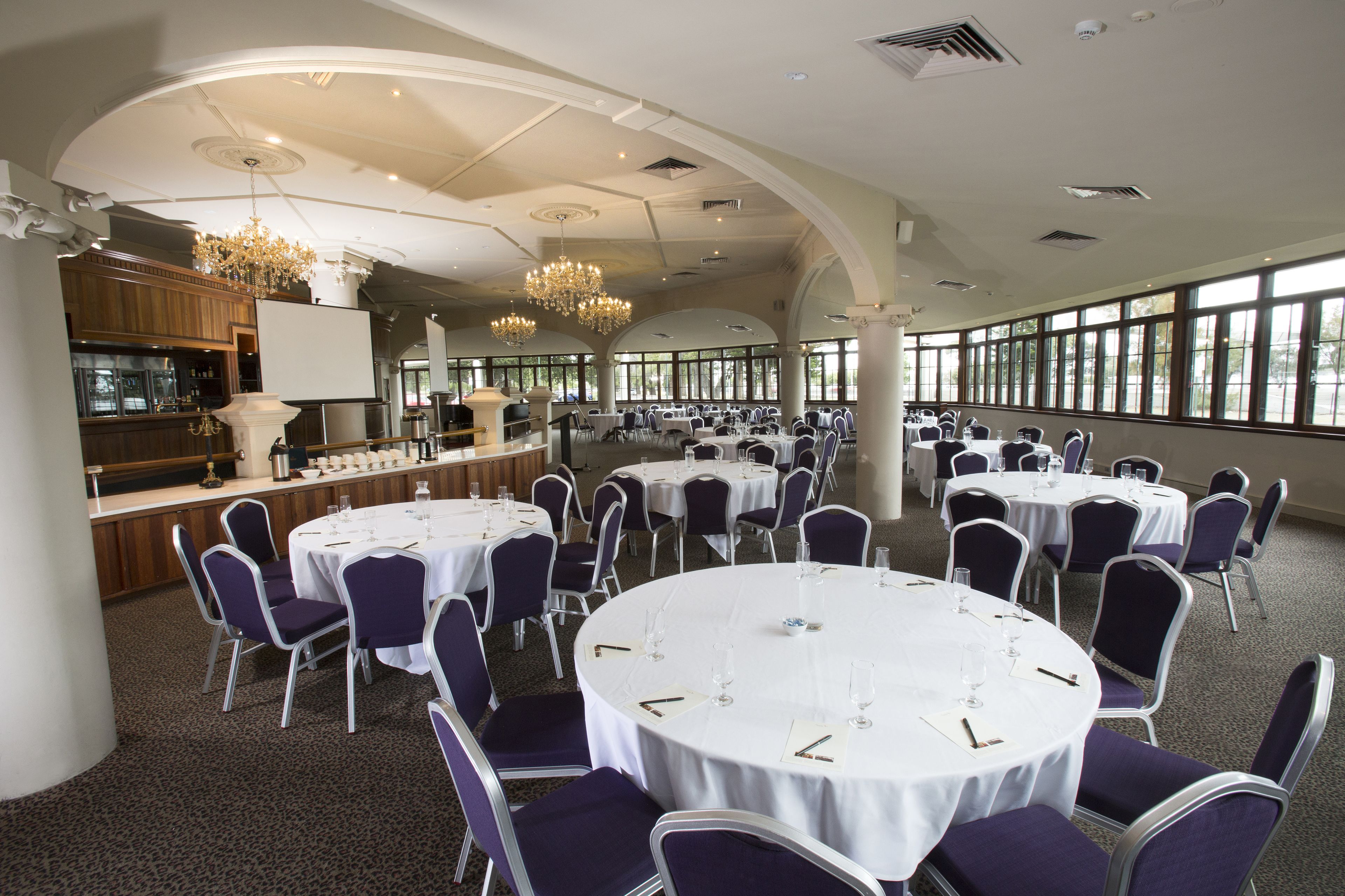 Un salón de banquetes con varias mesas redondas, cada una cubierta con manteles blancos y sillas moradas.