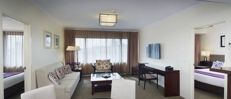 A hotel room with a bed, a sofa, a desk, a coffee table, and a TV.