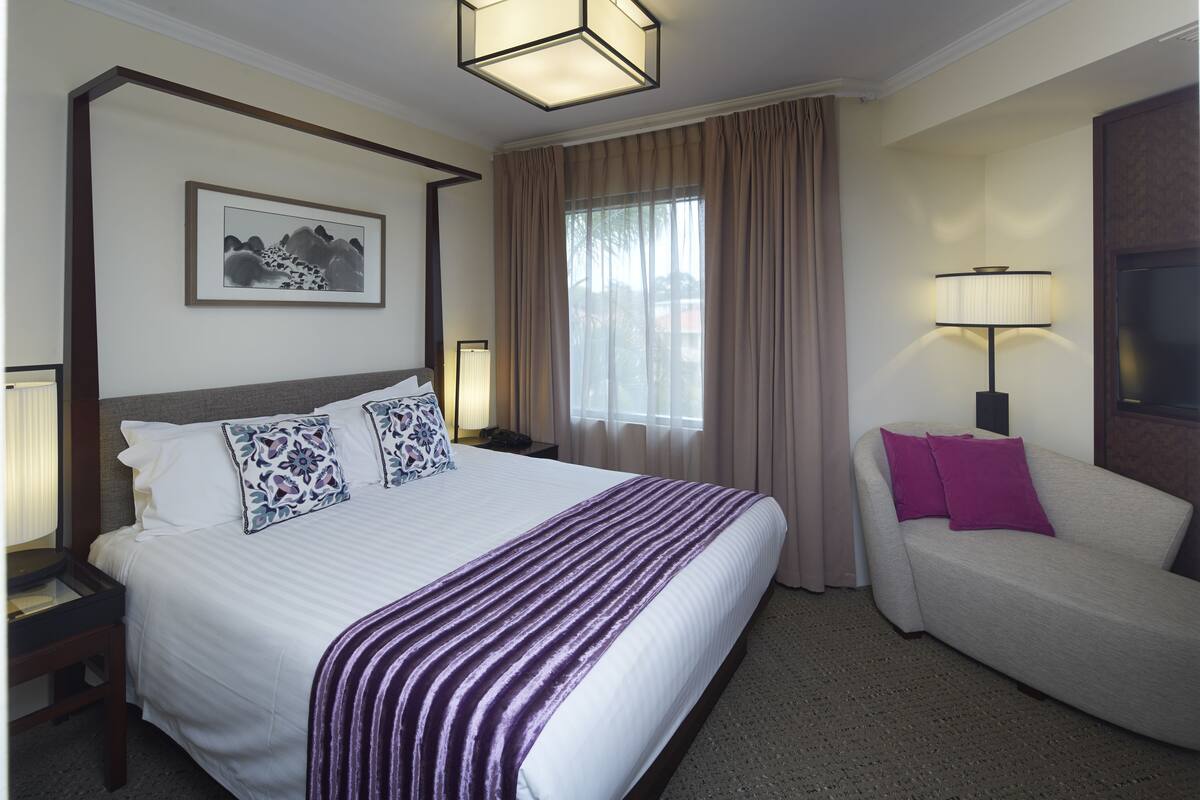 A hotel room with a large bed, a sofa, a nightstand, a lamp, and a framed picture on the wall.