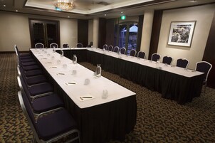 Una sala conferenze con un lungo tavolo, sedie e pavimento rivestito di moquette.