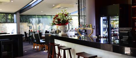 Un área de bar moderna con encimera negra, taburetes de madera y un jarrón decorativo con flores.