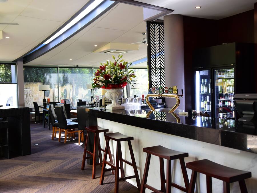 Un área de bar moderna con encimera negra, taburetes de madera y un jarrón decorativo con flores.