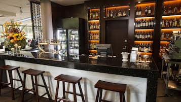 Angolo bar con un bancone in marmo, sgabelli di legno e scaffali pieni di bottiglie.