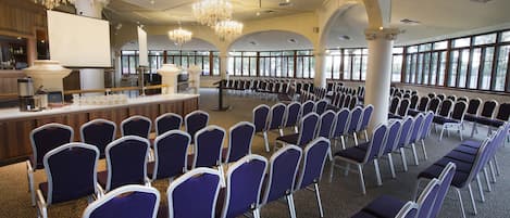 A conference room with rows of chairs, a podium, and a buffet area.