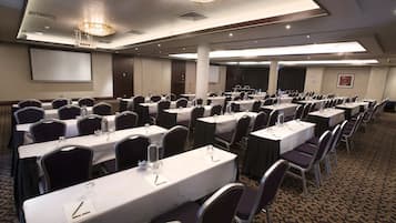 Un salón de conferencias con varias mesas, sillas y una pantalla para proyector.