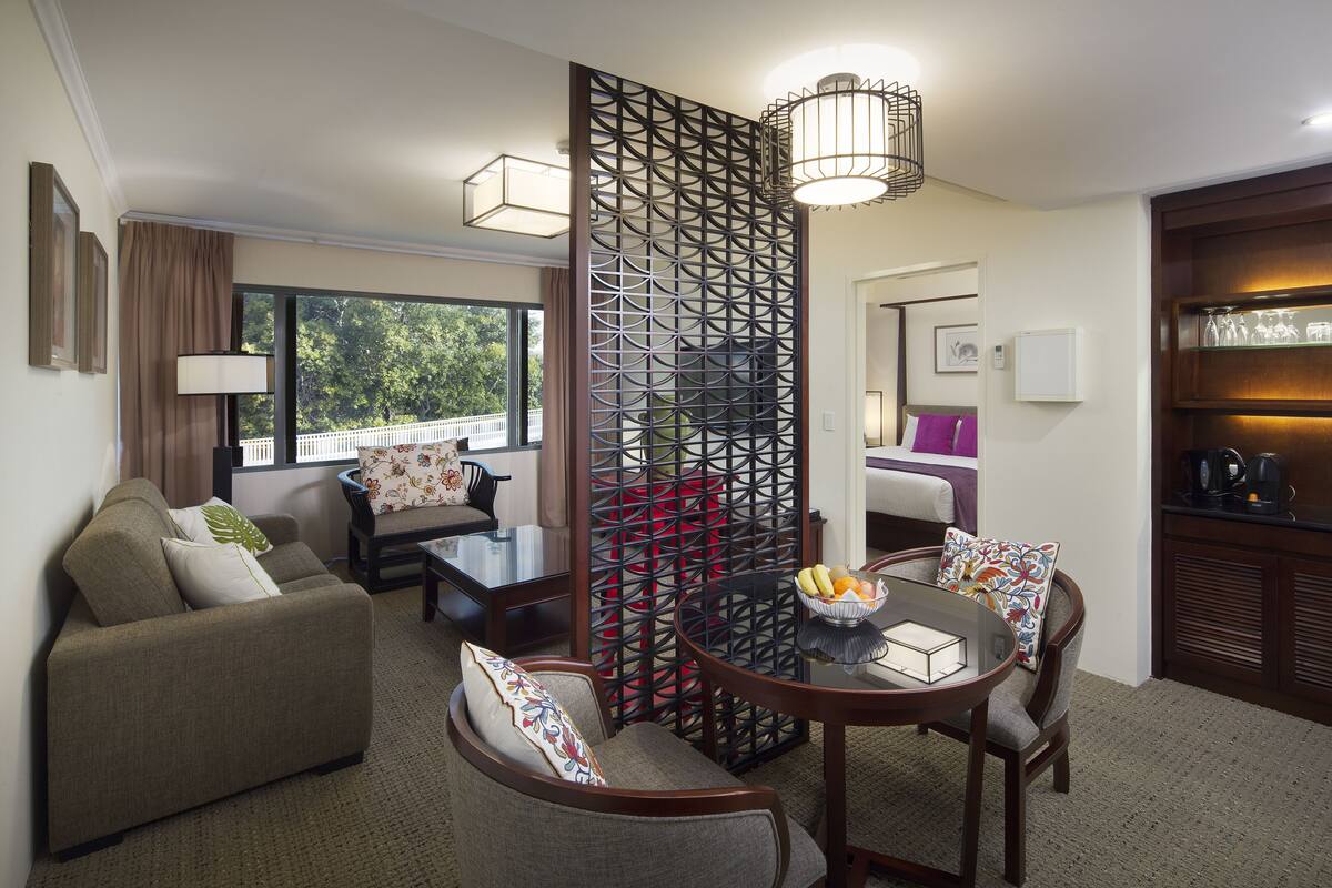 A modern living room with a sofa, a round table with a fruit bowl, a decorative partition, and a view of the outdoors.