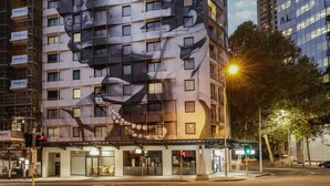 A building with a large mural of a face on its facade, multiple balconies, and a street-level entrance with shops. - Wyndham Suites Sydney (Sydney)