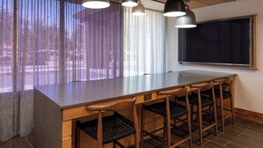 Zona de bar con una barra alargada, cuatro taburetes de madera y un ventanal con cortinas traslúcidas.